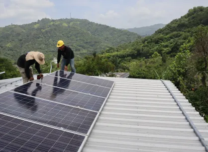 Two men install solar panels on a roof with mountains in background.